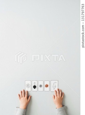 A child's hands with illustrated cards for a learning game or psychological test. Top view flat lay for early education and childhood development concepts. Minimalist composition with copy space A child's hands with illustrated cards for a learning game or psychological test. Top view flat lay for early education and childhood development concepts. Minimalist composition with copy space 131797763