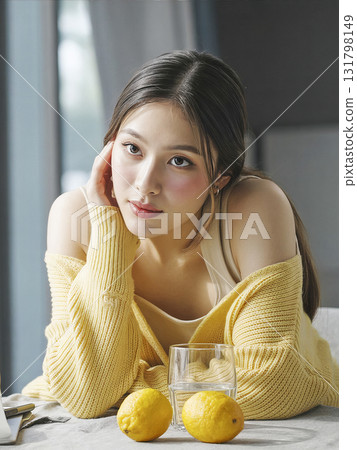 Woman is sitting on a table with a glass of water and two lemons Woman is sitting on a table with a glass of water and two lemons 131798149