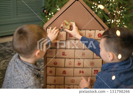 On a December morning, children check the gift compartments in the Advent calendar. The brothers are waiting for the new year On a December morning, children check the gift compartments in the Advent calendar. The brothers are waiting for the new year 131798266