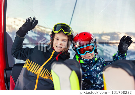 Portrait of two happy kid boys enjoy having fun sit ski lift gondola at alpine mountain skiing resort on bright winter day. Teen beginner skier rest of training in ski school Portrait of two happy kid boys enjoy having fun sit ski lift gondola at alpine mountain skiing resort on bright winter day. Teen beginner skier rest of training in ski school 131798282