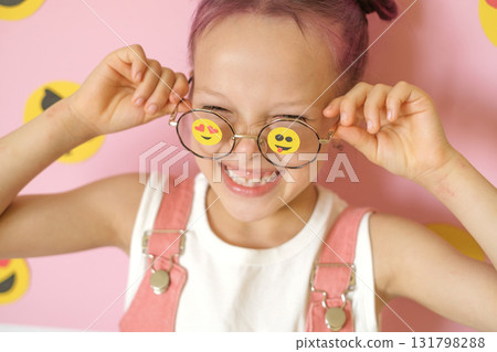 Funny Humorous laughing girl with smiley icons pasted on glasses. World Social Media Day. The problem of children's involvement in cyberspace. Funny Humorous laughing girl with smiley icons pasted on glasses. World Social Media Day. The problem of children's involvement in cyberspace. 131798288