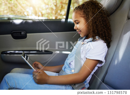 Happy, road trip and a child in a car with a tablet for a movie, cartoons or video. Smile, travel and a girl sitting in a vehicle with tech, streaming online and enjoying a film for entertainment 131798578