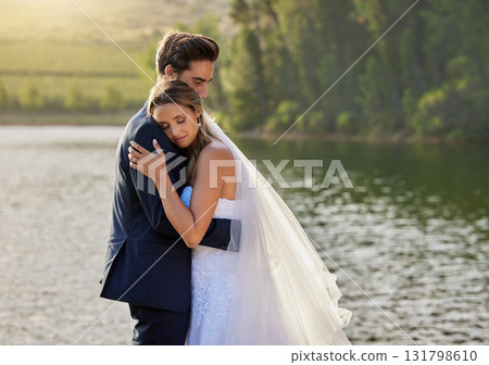 Wedding couple, hug and relax by lake for love on romantic getaway or honeymoon in nature. Calm woman hugging man in happy marriage relaxing by the water together enjoying the loving embrace outdoors 131798610