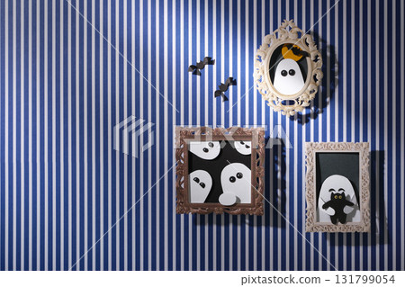 Handmade Halloween wall decorations: paper portraits of ghosts and bats in frames against a blue and white striped background. Space for your text. Handmade Halloween wall decorations: paper portraits of ghosts and bats in frames against a blue and white striped background. Space for your text. 131799054