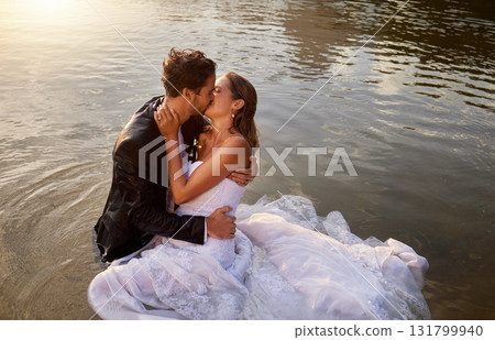 Wedding, kiss and couple in the water of a lake to celebrate their sunset marriage outdoor in nature. Happy, love and young wet man and woman being intimate for romantic playful outdoor celebration. Wedding, kiss and couple in the water of a lake to celebrate their sunset marriage outdoor in nature. Happy, love and young wet man and woman being intimate for romantic playful outdoor celebration. 131799940
