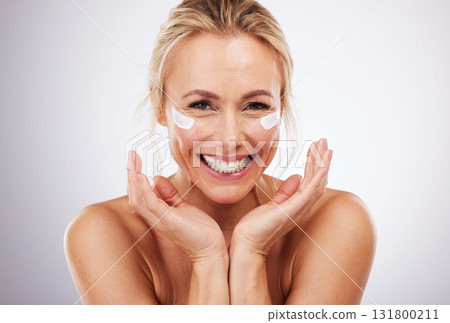 Skincare, eye cream and portrait of mature woman, anti ageing treatment and isolated on grey studio background. Health, skin and model face with smile and collagen mask on eyes in luxury spa facial. Skincare, eye cream and portrait of mature woman, anti ageing treatment and isolated on grey studio background. Health, skin and model face with smile and collagen mask on eyes in luxury spa facial. 131800211