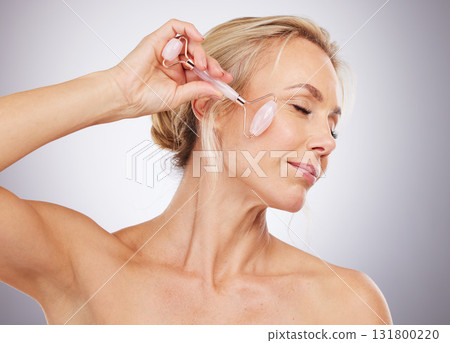 Woman, roller and skincare for cosmetics, anti aging or facial treatment against a gray studio background. Happy mature female model with rolling tool for beauty aesthetic, wellness or dermatology 131800220