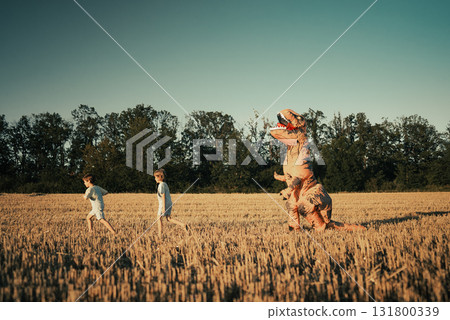 Funny scene of children running from dinosaur T-Rex in field. Cosplay Halloween Funny scene of children running from dinosaur T-Rex in field. Cosplay Halloween 131800339