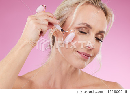 Face roller, beauty and woman facial massage with dermatology and cosmetic tools. Happy mature person on pink background for skincare, self care and rose quartz results for anti aging, glow and shine 131800946