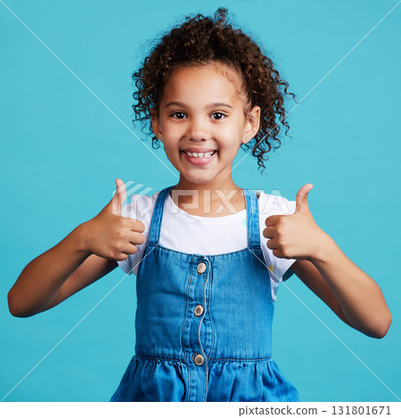 Smile thumbs up and portrait of a kid in a studio with success, happiness and achievement. Happy, positive and face of a girl child with a satisfaction or approval hand gesture by a blue background. Smile thumbs up and portrait of a kid in a studio with success, happiness and achievement. Happy, positive and face of a girl child with a satisfaction or approval hand gesture by a blue background. 131801671
