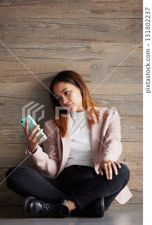 Young business woman, floor and texting with bored face on social media, app or phone in modern office. Professional female, smartphone and tired with search for email, chat or communication on break 131802237