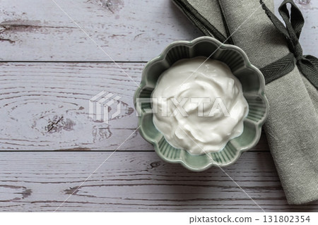 Natural white greek yogurt in porcelain green plate on the wood table with green napkin for healthy breakfast. Food concept. Space for text. 131802354
