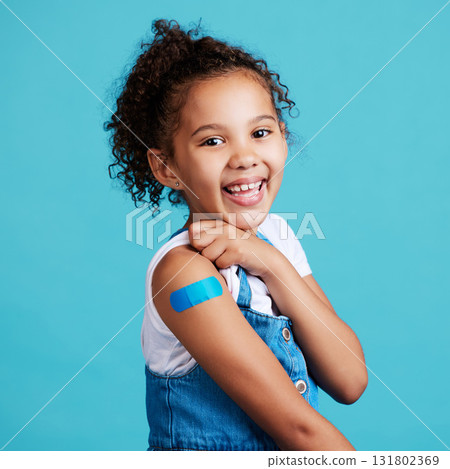 Portrait, smile and girl with plaster, wellness and safety with kid against a blue studio background. Face, young person and female child with happiness, band aid and vaccine with protection and care 131802369