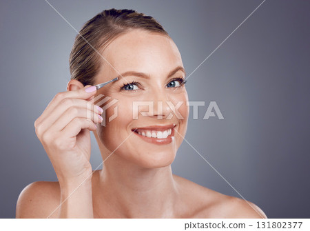 Eyebrows, grooming and portrait of a woman with a tweezers isolated on a grey studio background. Beauty, treatment and happy model plucking hair from face for shaping and routine on a backdrop 131802377