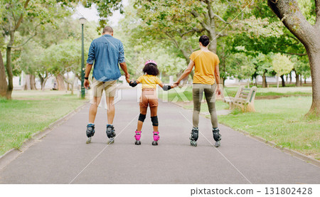 Family, park and holding hands to rollerskate with girl child with care, learning and support. Interracial parents, black man and woman with kid, back and helping hand on road for outdoor holiday 131802428