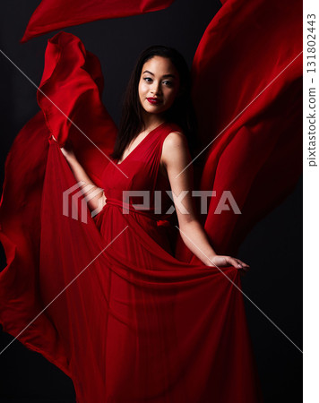 Portrait of woman, art and fashion, fabric on dark background with beauty and aesthetic movement. Flowing silk motion, fantasy and artistic model with smile in red creative designer dress in studio. Portrait of woman, art and fashion, fabric on dark background with beauty and aesthetic movement. Flowing silk motion, fantasy and artistic model with smile in red creative designer dress in studio. 131802443