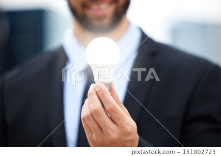 Businessman, hands and light bulb with idea in the city for solution, eco friendly or renewable energy. Hand of male employee holding lamp for creativity, ideas or power saving element on mockup 131802723
