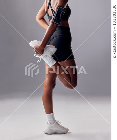 Fitness, health and woman stretching in a studio before a workout, running or sport training. Sports, wellness and closeup back view of female athlete doing a leg warm up exercise by gray background. 131803530