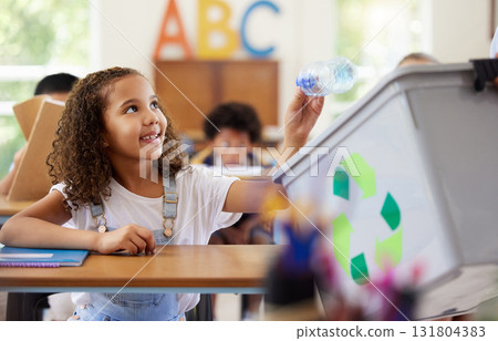 Learning, recycle bin and girl in classroom throwing trash for cleaning, climate change or eco friendly in school. Recycling plastic, smile and education with happy student or kid in kindergarten. 131804383
