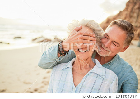 Love, happy and surprise with old couple on beach for anniversary, celebration and vacation. Travel, relax and smile with senior man cover eyes of woman for retirement, summer and support in nature 131804387
