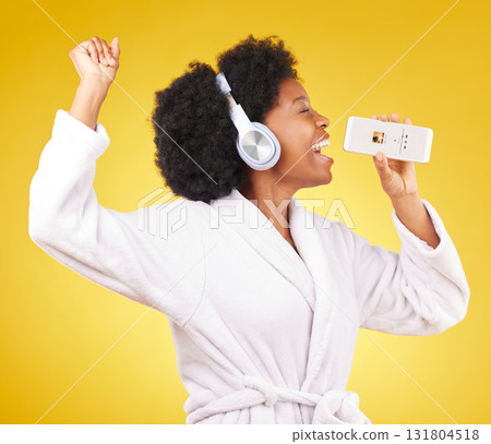 Black woman, music headphones and singing with phone in studio isolated on a yellow background. Karaoke singer, bathrobe and happy female dance with mobile microphone while streaming podcast or radio 131804518