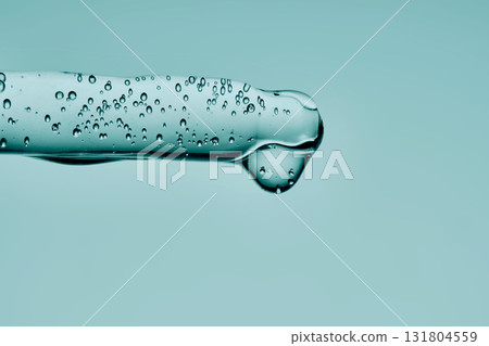 A drop of serum drips from a pipette on a delicate green background. A drop of serum drips from a pipette on a delicate green background. 131804559