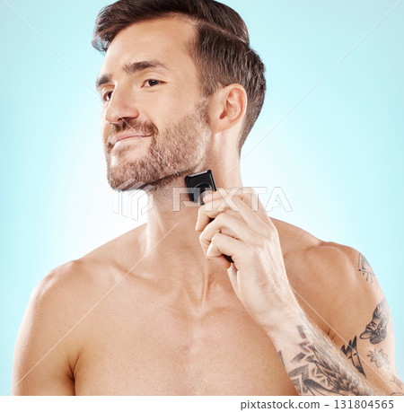 Man, beard and shaving with trimmer in studio isolated on a blue background for hair removal. Haircare thinking, grooming and male model with electric shaver to shave for hygiene, health or wellness. 131804565