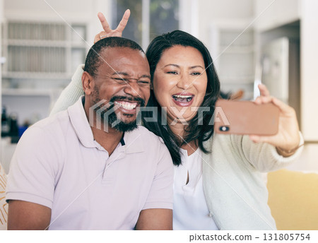 Senior black couple, selfie or happy in home together for silly, social media or relax with peace sign hand. Mature man, woman and digital photography app in house for embrace, bonding and bunny ears Senior black couple, selfie or happy in home together for silly, social media or relax with peace sign hand. Mature man, woman and digital photography app in house for embrace, bonding and bunny ears 131805754