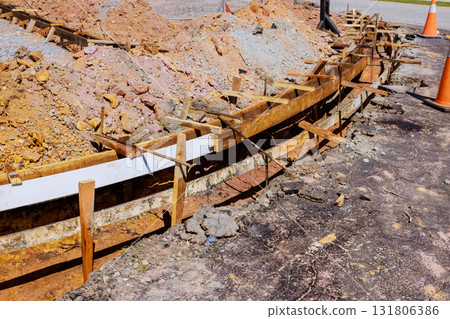 Workers prepare for curbed concrete installation at construction site with compacted soil wooden forms. 131806386