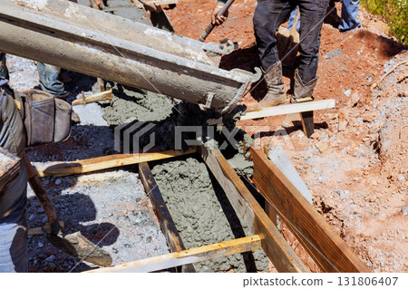 Skilled laborers are pouring concrete into wooden frames, shaping curbed foundation 131806407