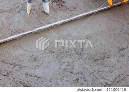 Workers smooth wet cement on construction site during concrete works preparing for flooring installation. 131806416