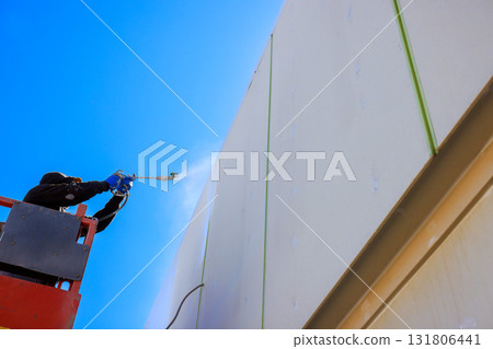 Painter applies paint to building wall from high lift on works day Painter applies paint to building wall from high lift on works day 131806441