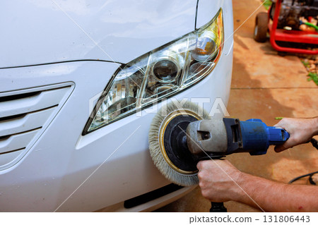 Worker hold polishing machine as someone shines front of white car 131806443