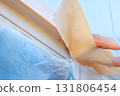 Painter gently peel away masking tape from window trim, revealing freshly painted surfaces during home renovation. 131806454