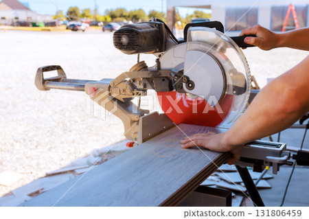 Carpenter operates miter saw to cut wood planks in construction area, focusing on precision. 131806459