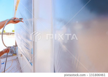 Worker is spray painting exterior of building while covered in protective plastic sheeting. Worker is spray painting exterior of building while covered in protective plastic sheeting. 131806461
