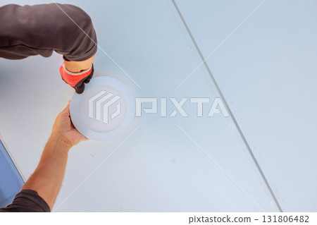 Worker wearing gloves is placing round light fixture onto ceiling Worker wearing gloves is placing round light fixture onto ceiling 131806482