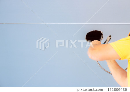 Electrician reaches into ceiling hole to work on electrical wires during renovation in abuilding. 131806486