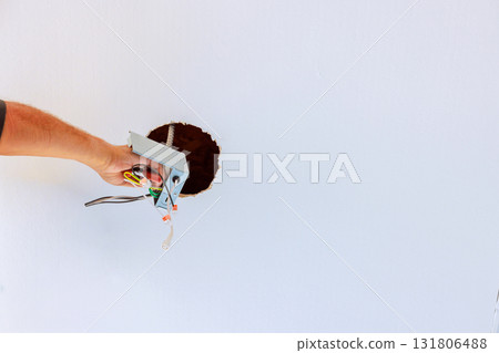 Electricians is reaching through hole in ceiling, working on electrical wires during home repairs. Electricians is reaching through hole in ceiling, working on electrical wires during home repairs. 131806488