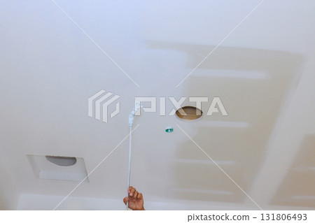 Painter is engaging in ceiling paints by reaching up with spray tool towards surface above. Painter is engaging in ceiling paints by reaching up with spray tool towards surface above. 131806493
