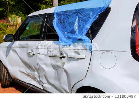 White car with significant damage bears blue plastic on broken window 131806497
