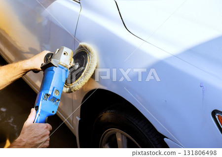 Person uses an electric polisher on white car surface to restore its shine during work day. 131806498