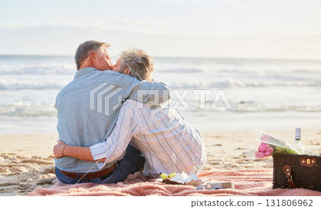 Senior couple, beach picnic and kiss with hug, romance and happiness in summer for anniversary celebration. Elderly man, old woman and basket for food, wine and outdoor for sunshine, waves and love 131806962