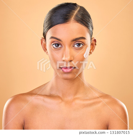 Face portrait, skincare and woman with cream in studio isolated on brown background. Dermatology, serious cosmetics and confident Indian female model with lotion, creme or moisturizer for skin health 131807015
