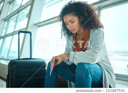 Airport, black woman and watch time check of a young female at plane terminal with flight delay. Waiting, sitting and person with passport document looking at smartwatch for board and transport info 131807541