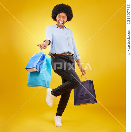 Black woman with shopping bag, happy with fashion and retail in portrait on yellow studio background. Happiness, female with discount and sale at boutique with designer brand, carefree and mockup Black woman with shopping bag, happy with fashion and retail in portrait on yellow studio background. Happiness, female with discount and sale at boutique with designer brand, carefree and mockup 131807758