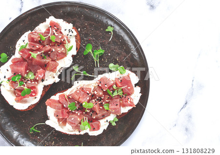 sandwiches, rye bread with cream cheese, sliced tuna fillet with herbs, breakfast on a black plate, homemade, 131808229