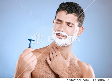 Shaving, beard and confused man with razor in hand, foam product placement in studio mock up. Shave accident, cream on face and hair or skincare for male model grooming, isolated on blue background. Shaving, beard and confused man with razor in hand, foam product placement in studio mock up. Shave accident, cream on face and hair or skincare for male model grooming, isolated on blue background. 131808284