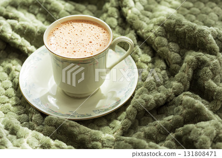 Frothy Coffee in Floral Cup on Cozy Green Blanket Frothy Coffee in Floral Cup on Cozy Green Blanket 131808471