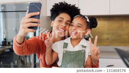 Mom, girl and selfie in kitchen, peace sign and smile with funny face, memory and post on web. Photography, mother and daughter with baking, learning or happy with food, social media or flour on nose Mom, girl and selfie in kitchen, peace sign and smile with funny face, memory and post on web. Photography, mother and daughter with baking, learning or happy with food, social media or flour on nose 131808576